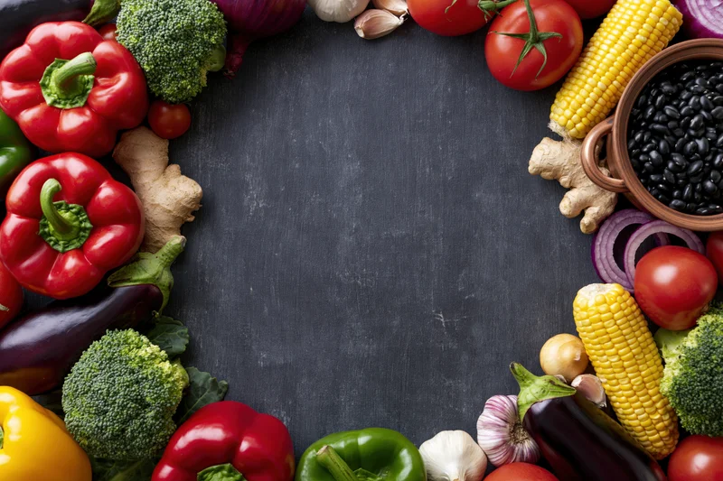 Fresh vegetables and legumes arranged in a border around a dark slate surface