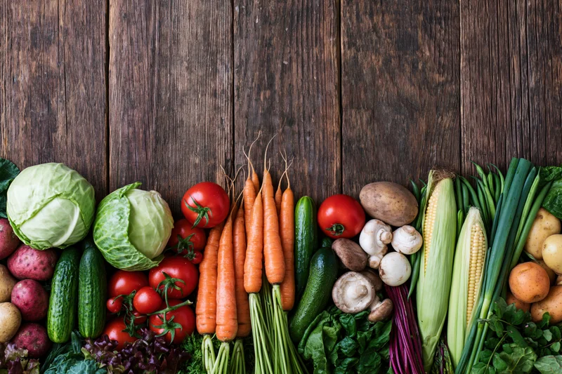 Assorted fresh vegetables arranged in a row along a wooden table with copyspace above