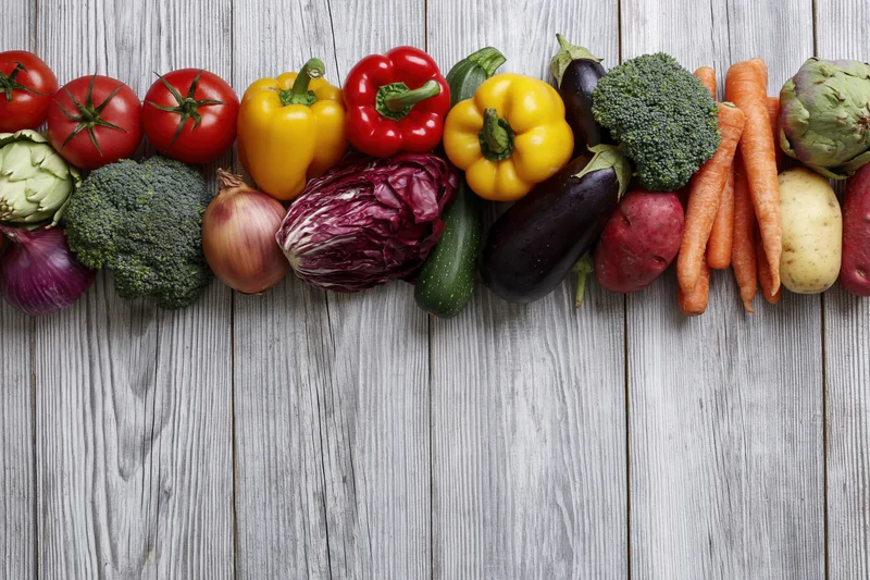 Assorted fresh vegetables arranged in a horizontal band across a wooden surface