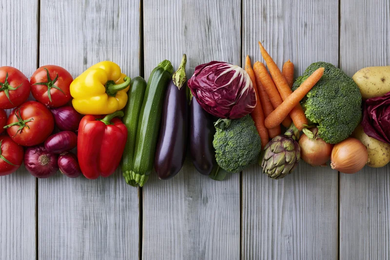 Assorted fresh vegetables arranged in a horizontal band across a wooden surface