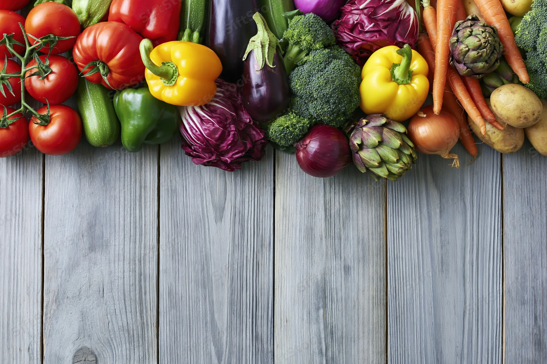 Assorted fresh vegetables arranged in a horizontal band across a gray wooden table