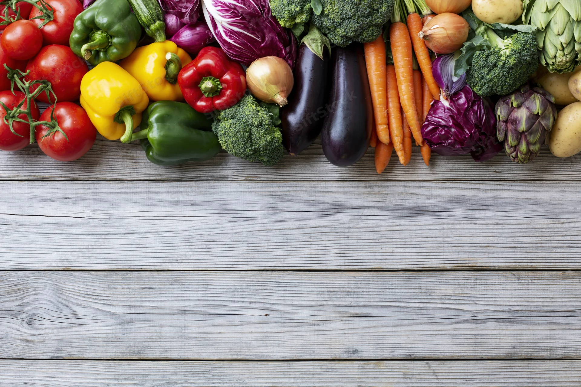 Assorted fresh vegetables arranged in a horizontal band across a weathered wooden table with copyspace below