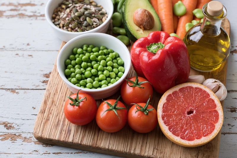 Fresh vegetables fruits seeds and olive oil arranged on a wooden cutting board