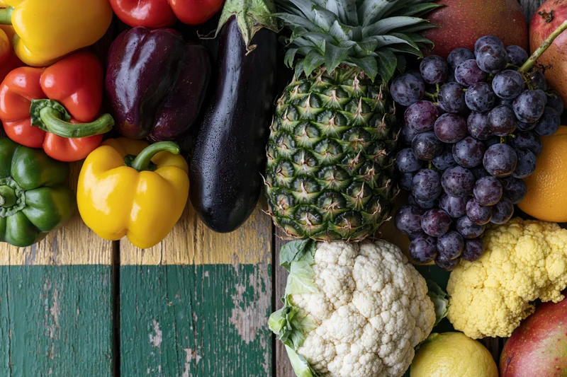 Assorted fresh vegetables and tropical fruits arranged on a rustic wooden surface