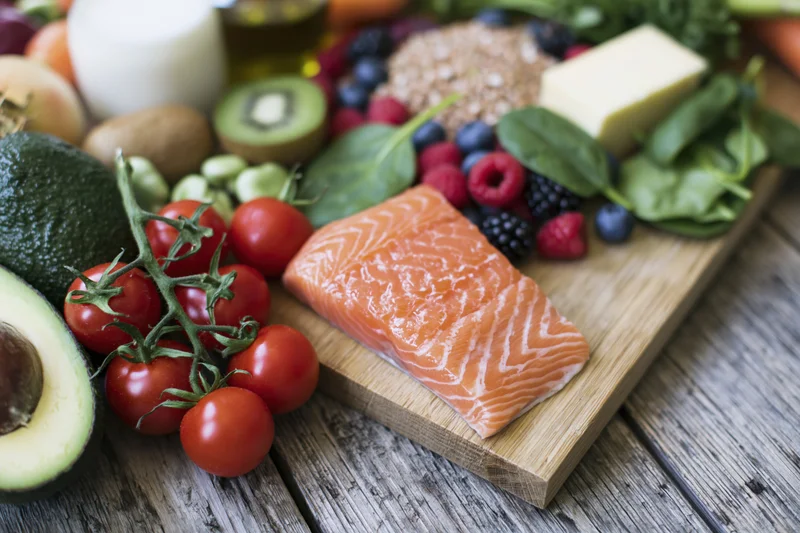 Raw salmon fillet with avocado, tomatoes, berries and greens arranged on a wooden cutting board