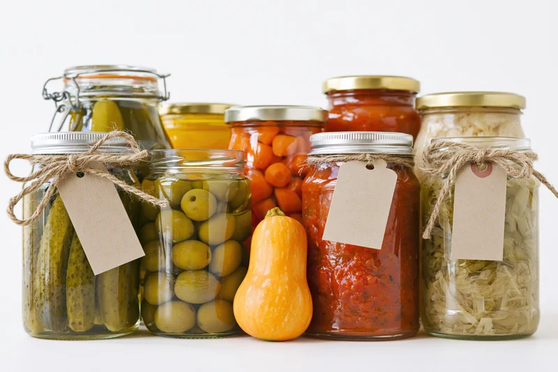 Glass jars filled with pickled and fermented vegetables arranged on a white surface with twine tags