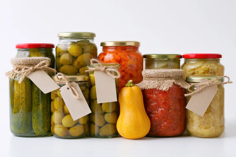 Assorted glass jars filled with pickled and preserved vegetables arranged on a white surface