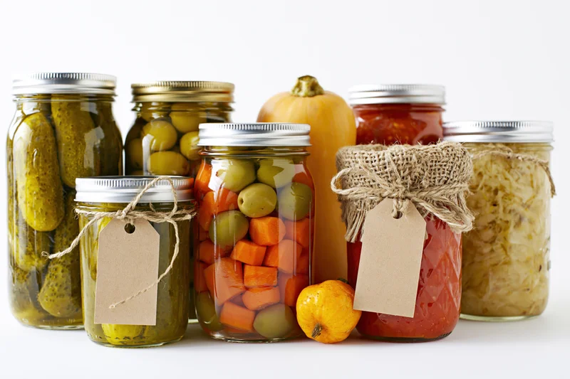 Glass jars filled with pickled and fermented vegetables arranged on a white surface