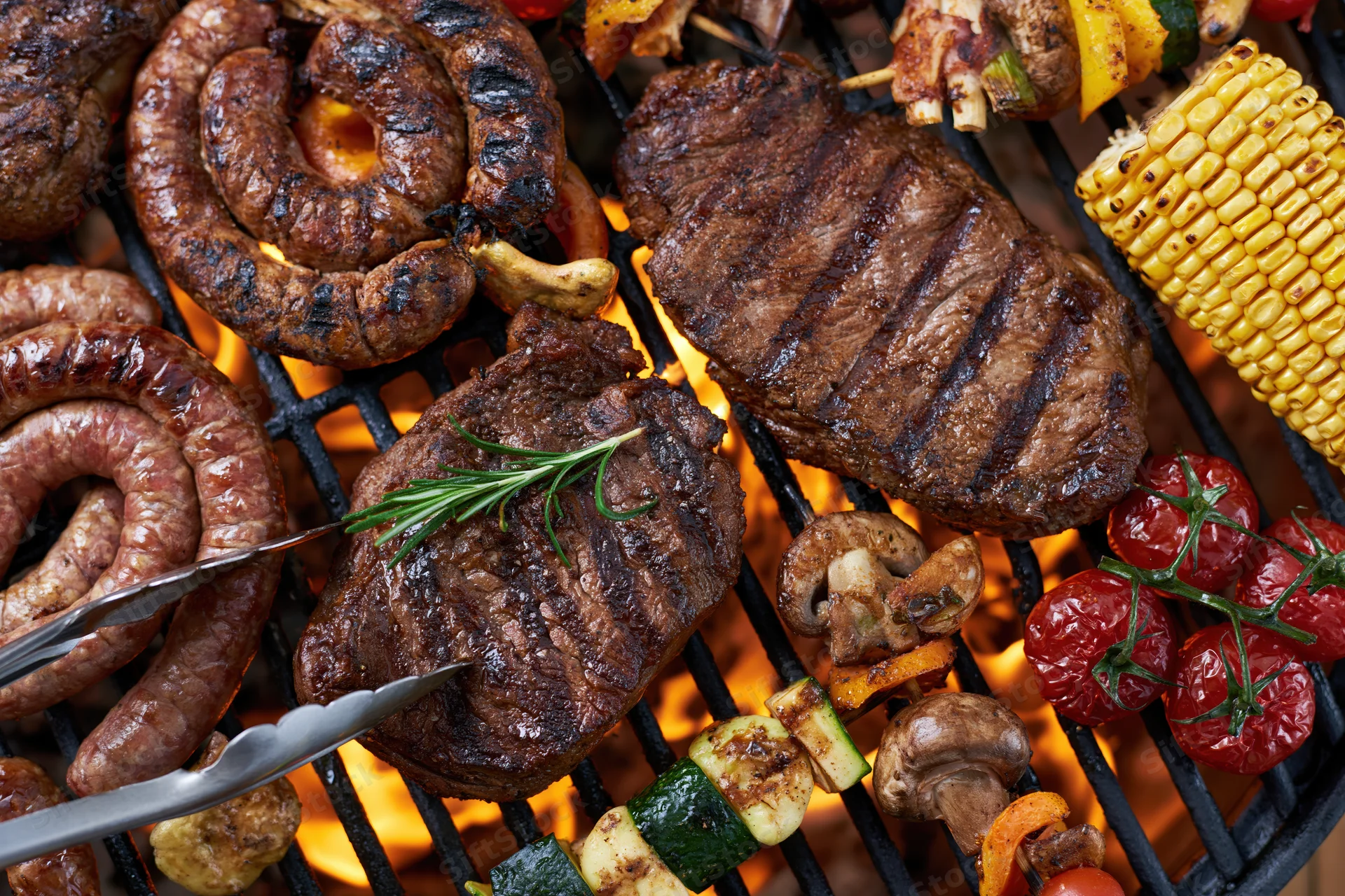 Assorted grilled meats and vegetables cooking on a flaming barbecue grill