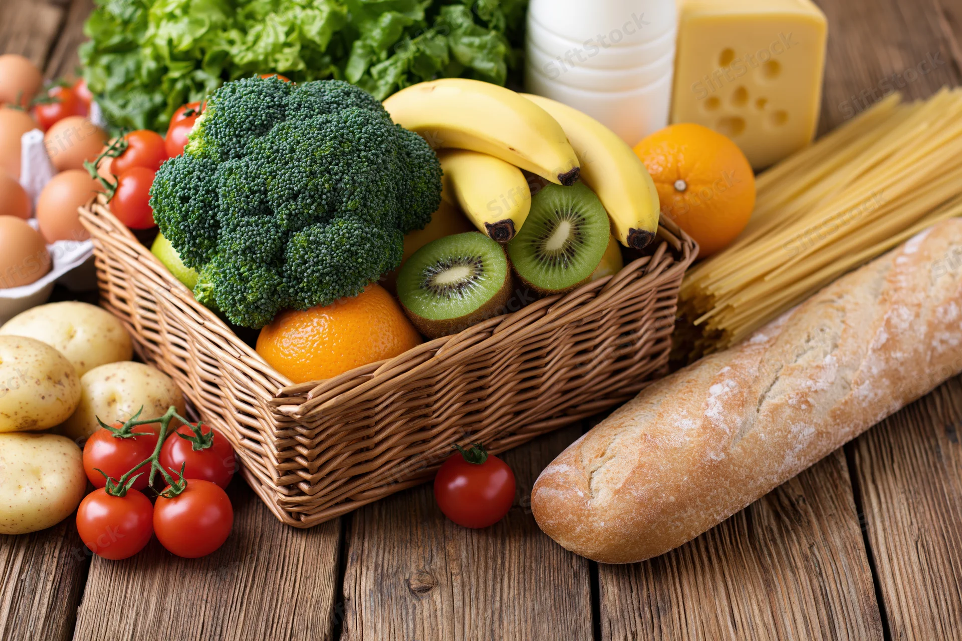 Assorted groceries arranged in a wicker basket on a rustic wooden table