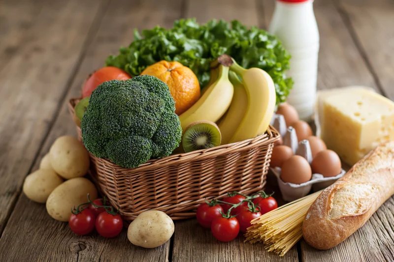 Assorted groceries arranged in a wicker basket on a rustic wooden table