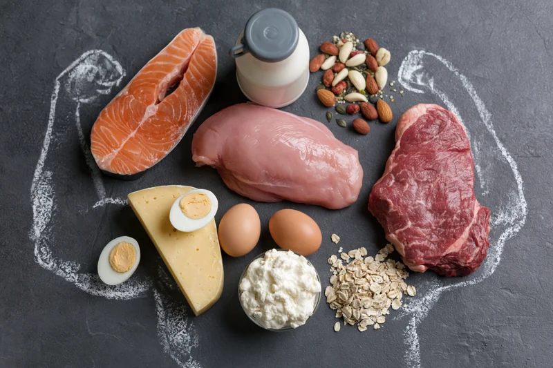 High-protein foods arranged in a muscular silhouette on dark chalkboard surface