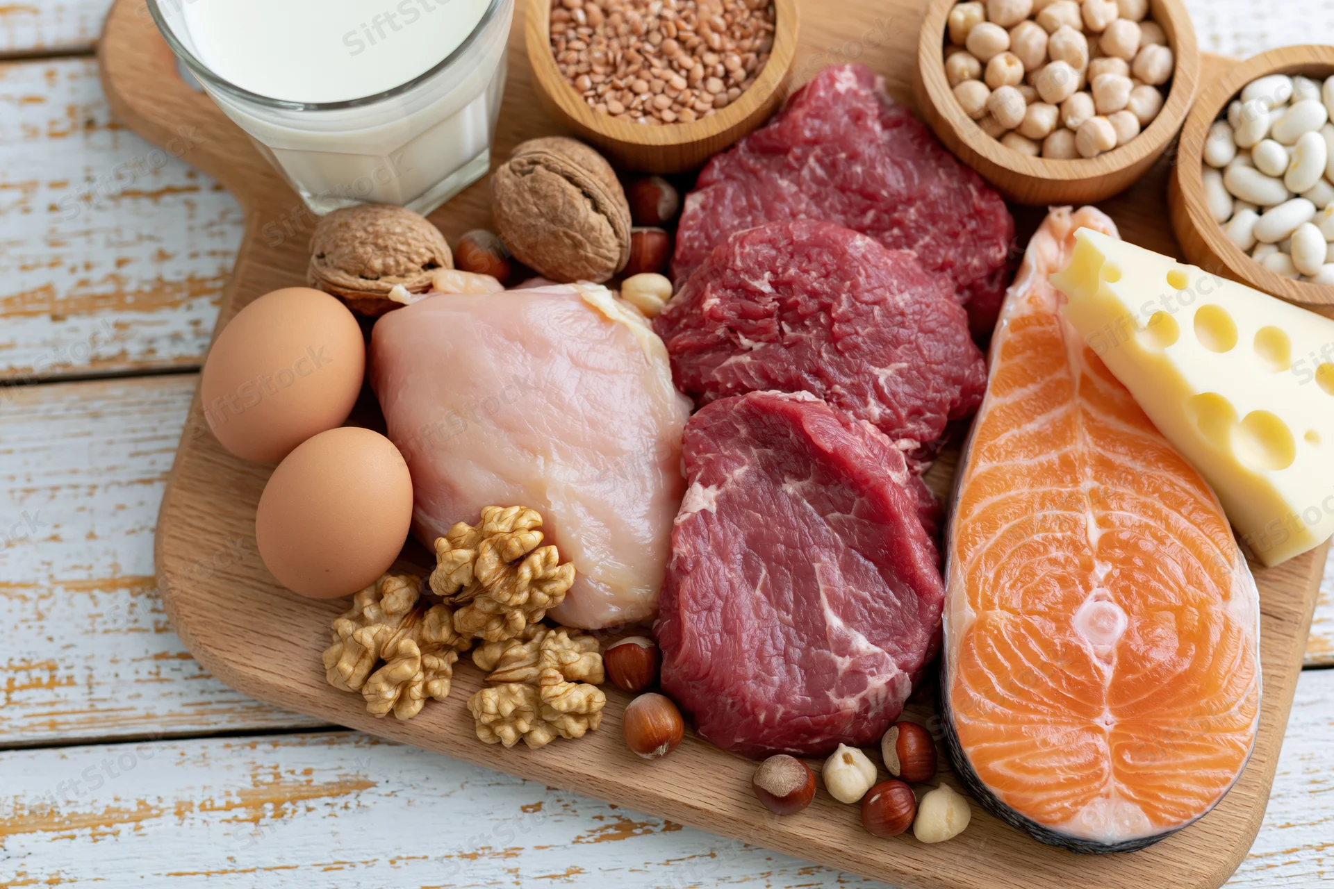 High-protein foods arranged on a wooden cutting board with meat, fish, eggs, dairy, nuts and legumes