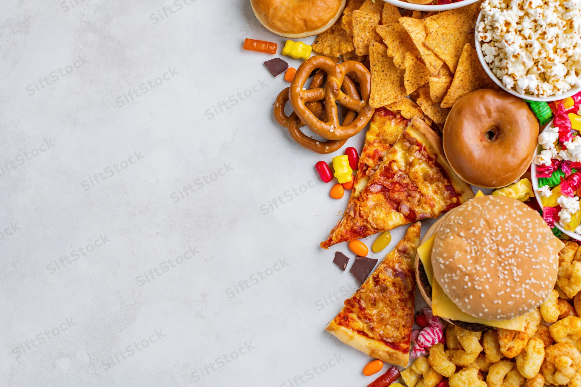 Assorted junk food and snacks arranged in diagonal border on white surface