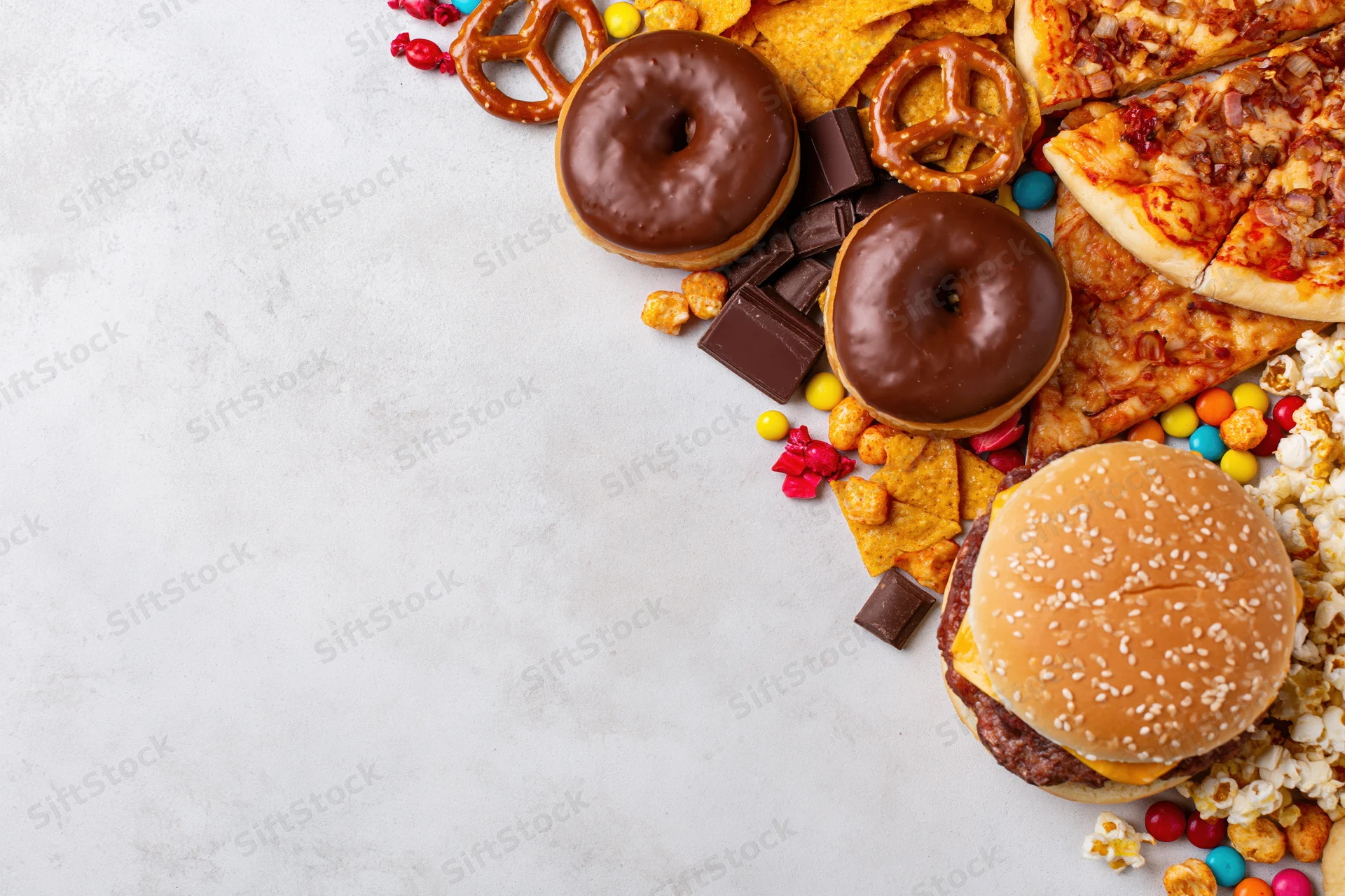 Assorted junk food and snacks arranged diagonally along the right side of a white surface with copyspace on the left