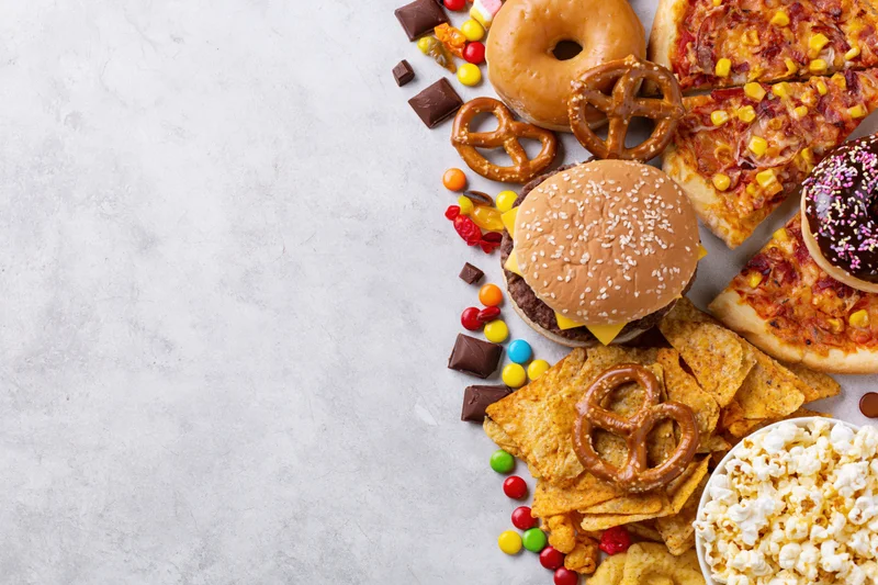 Assorted junk food and snacks arranged in diagonal border on light gray surface