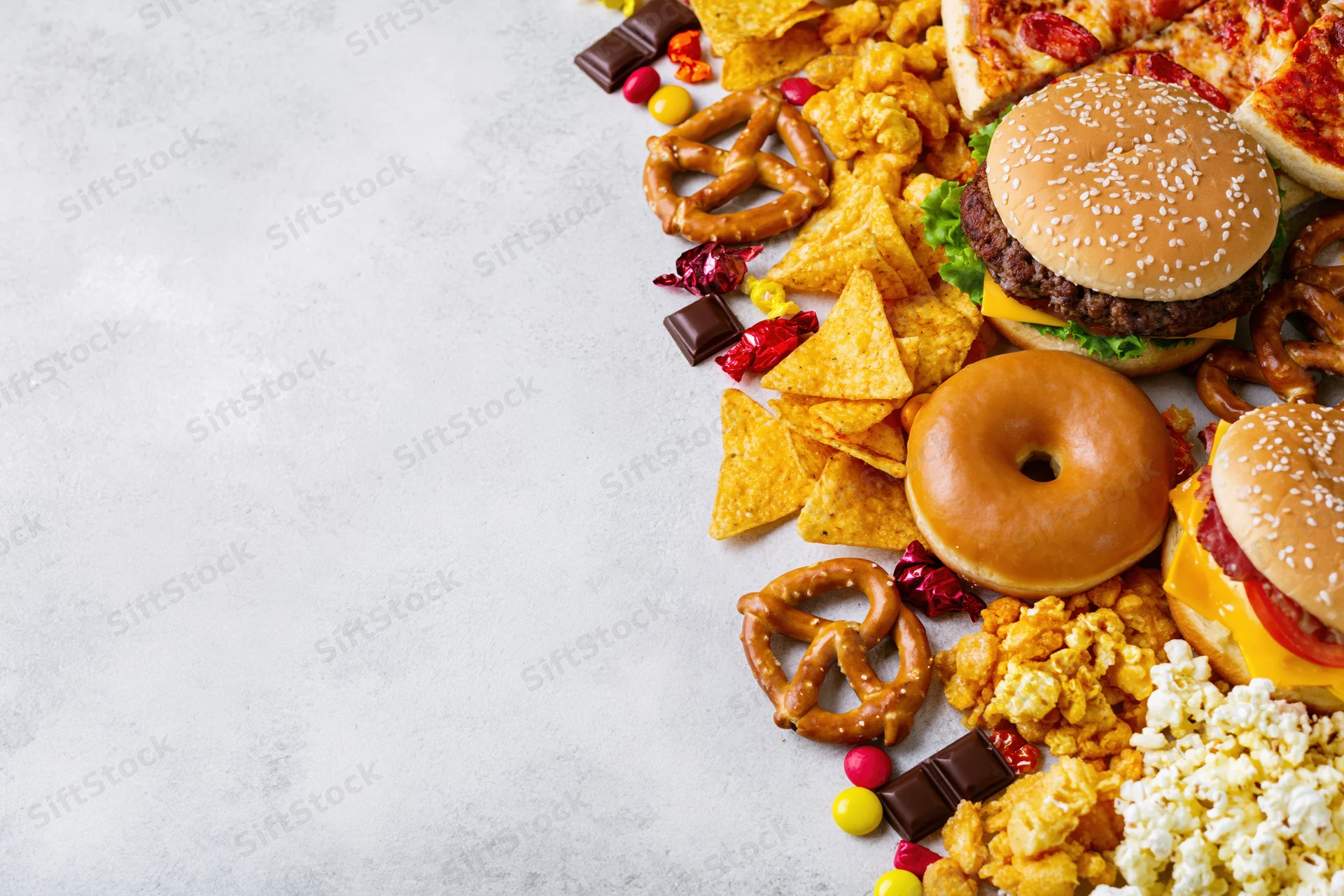 Assorted junk food and snacks arranged in diagonal border along right side of light surface