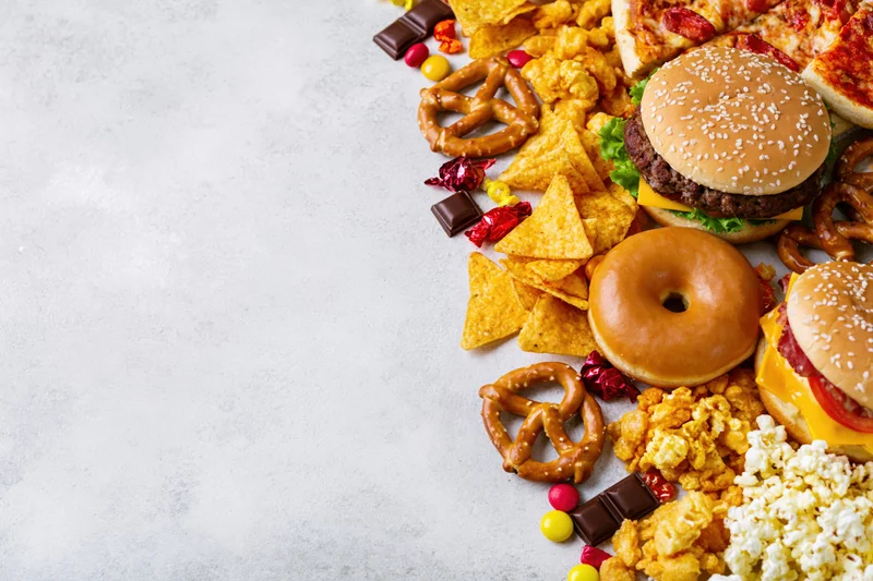 Assorted junk food and snacks arranged in diagonal border along right side of light surface
