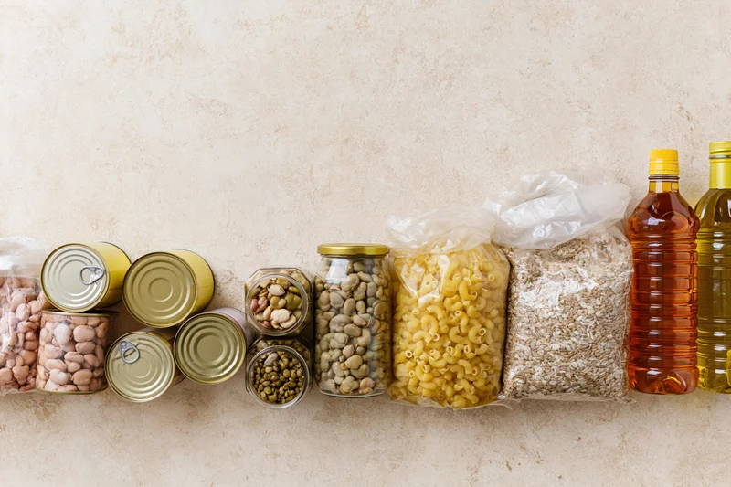 Assorted pantry staples arranged along the bottom edge of a textured beige wall