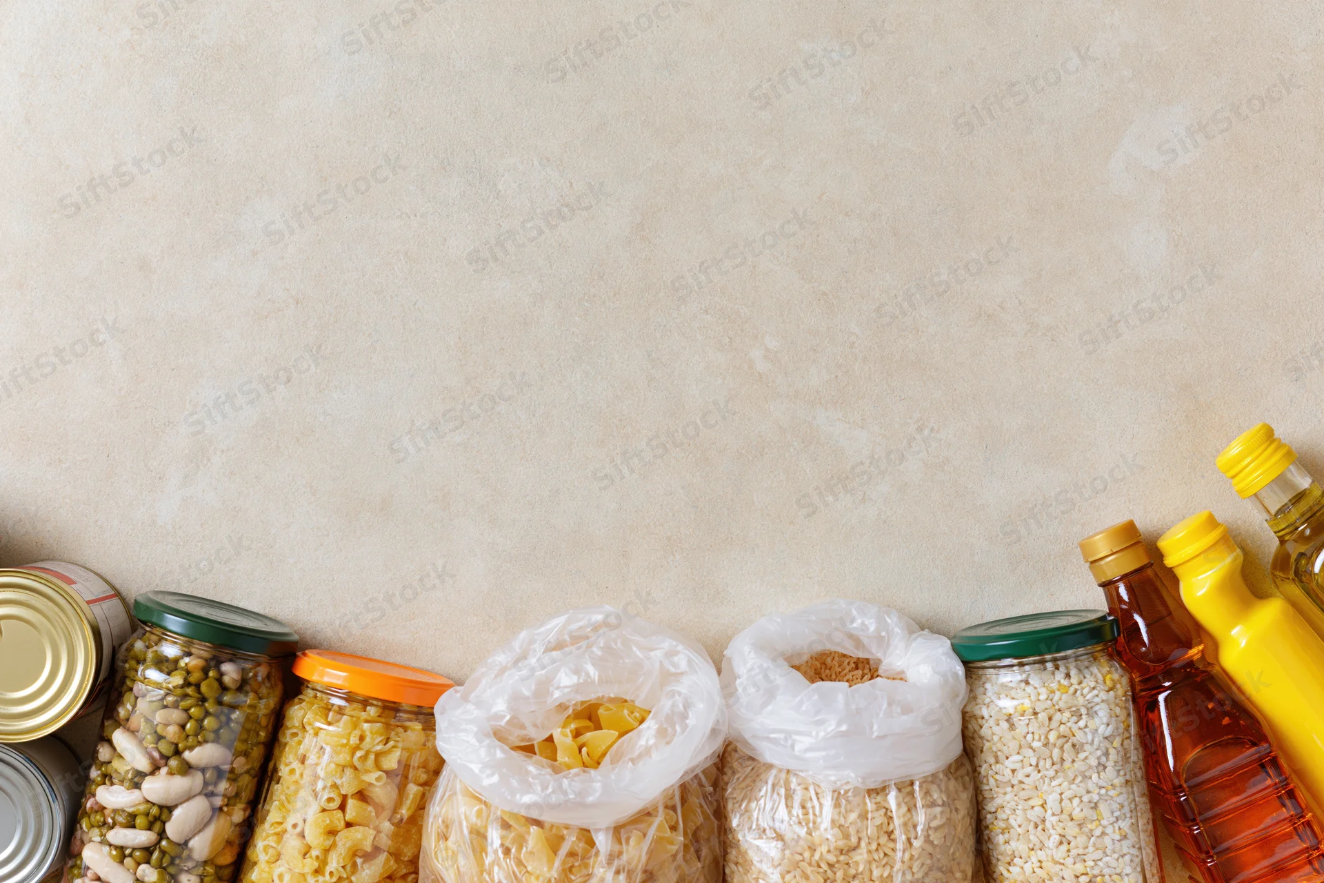 Assorted pantry staples arranged along the bottom edge of a textured beige wall