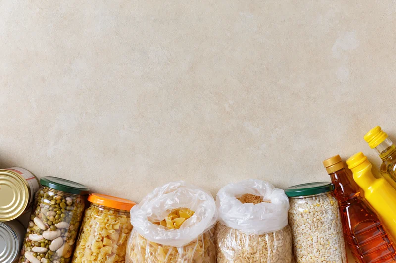Assorted pantry staples arranged along the bottom edge of a textured beige wall