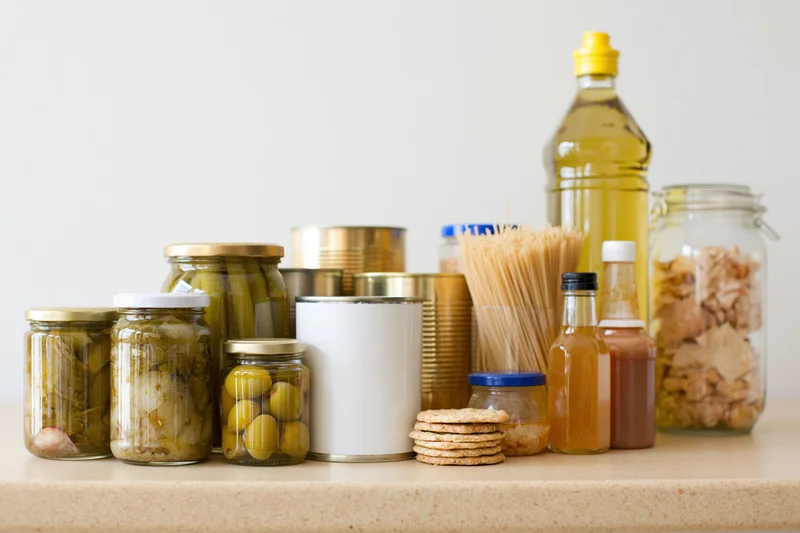 Assorted pantry staples arranged on a kitchen counter with jars, cans, and bottles of food and condiments