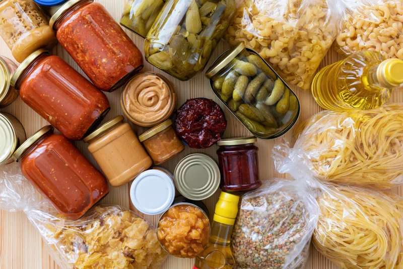 Assorted pantry staples densely arranged on a pale wooden surface