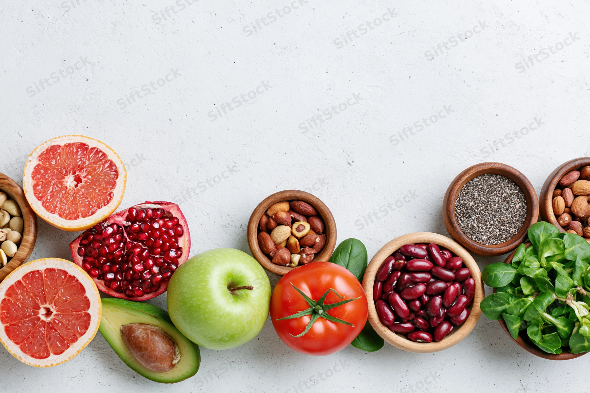 Assorted superfoods and fresh produce arranged in wooden bowls on a white surface