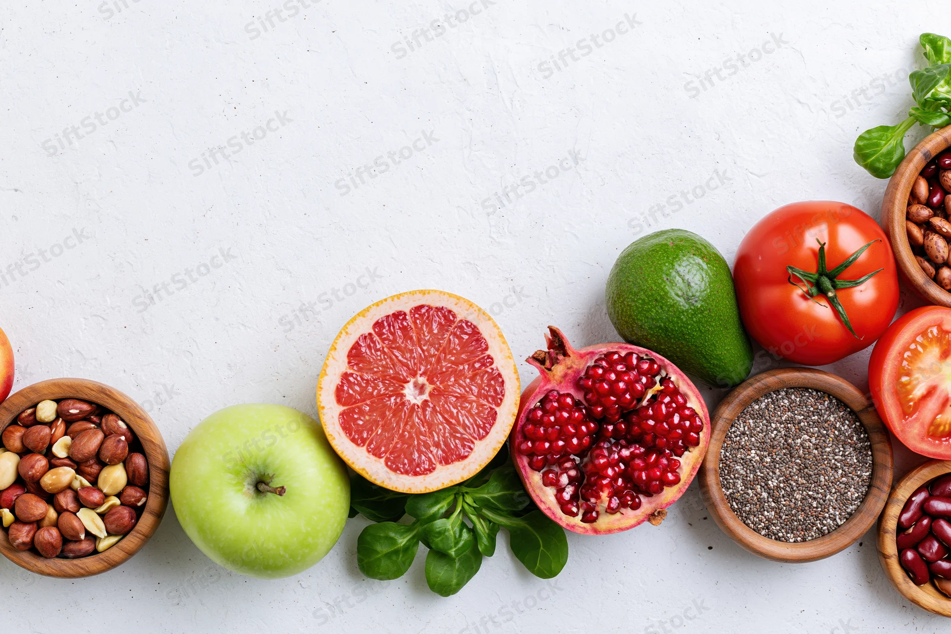 Assorted superfoods and fresh produce arranged along the bottom edge of a white surface in a flat lay composition