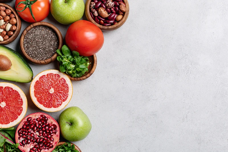Assorted superfoods and fresh produce arranged along the bottom left of a light countertop with copyspace on the right