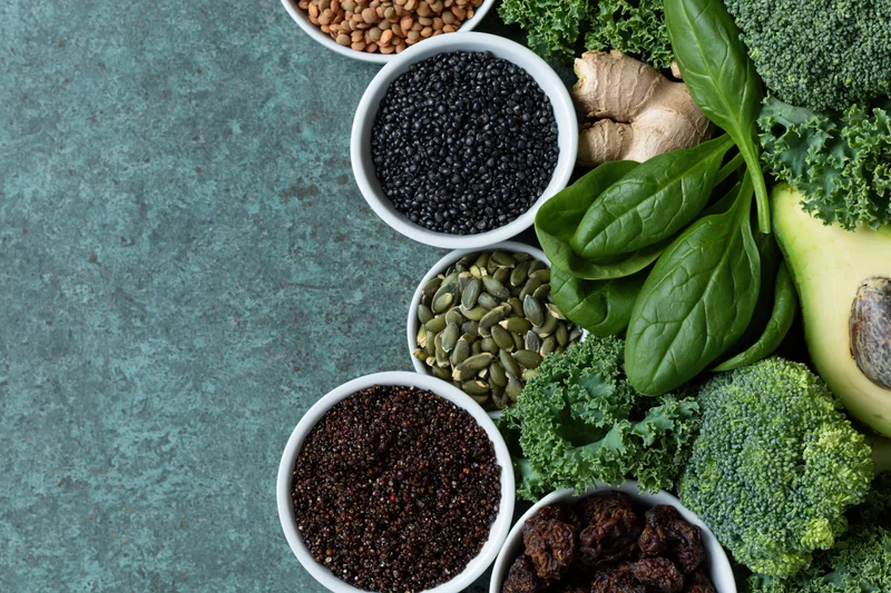 Superfoods and vegetables arranged along the right side of a textured blue surface with copyspace on the left