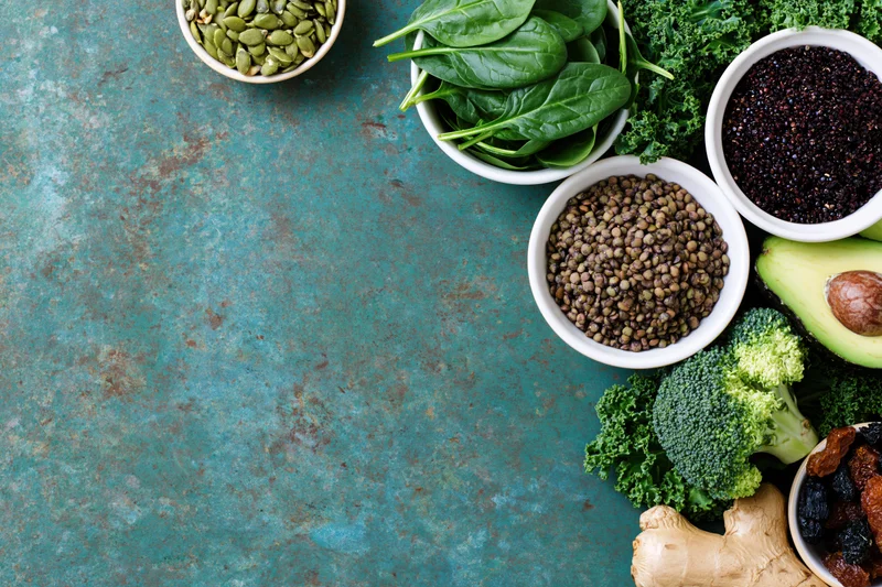 Assorted superfoods and vegetables arranged along the right side of a textured blue surface