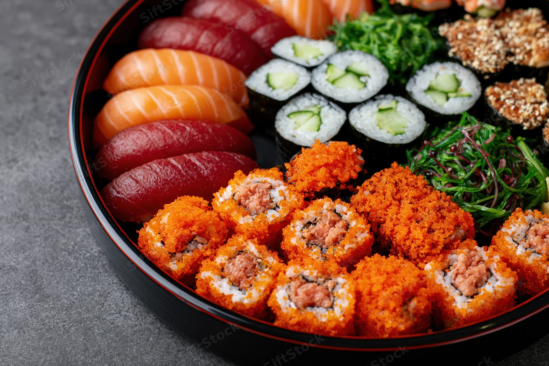 Assorted sushi platter arranged on a round black lacquer tray with sashimi, maki, and tobiko rolls