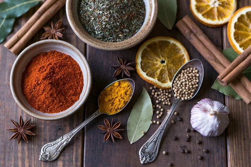 Assorted spices and herbs arranged in bowls and spoons on a dark wooden surface