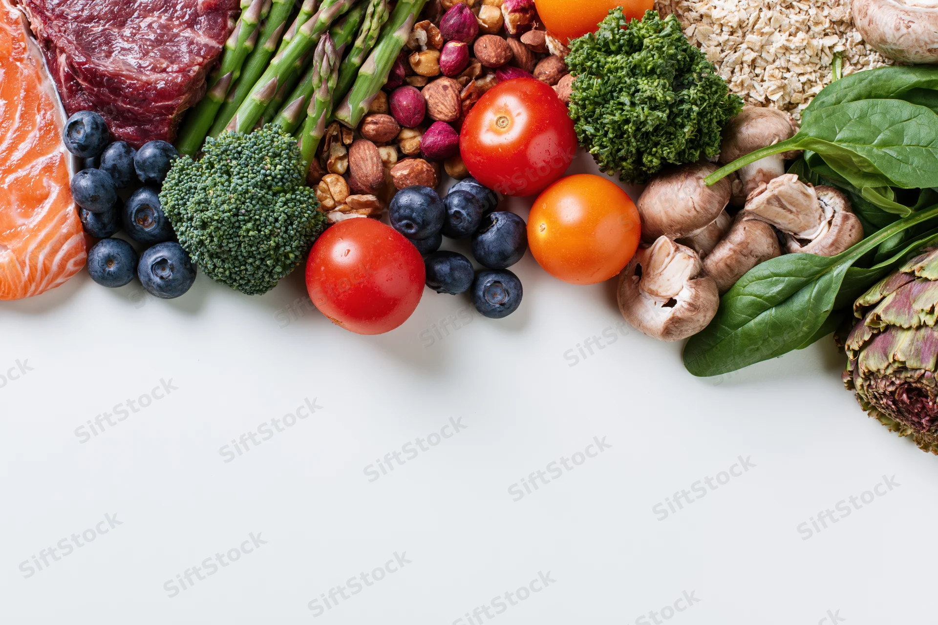Assorted whole foods arranged along bottom edge of white surface