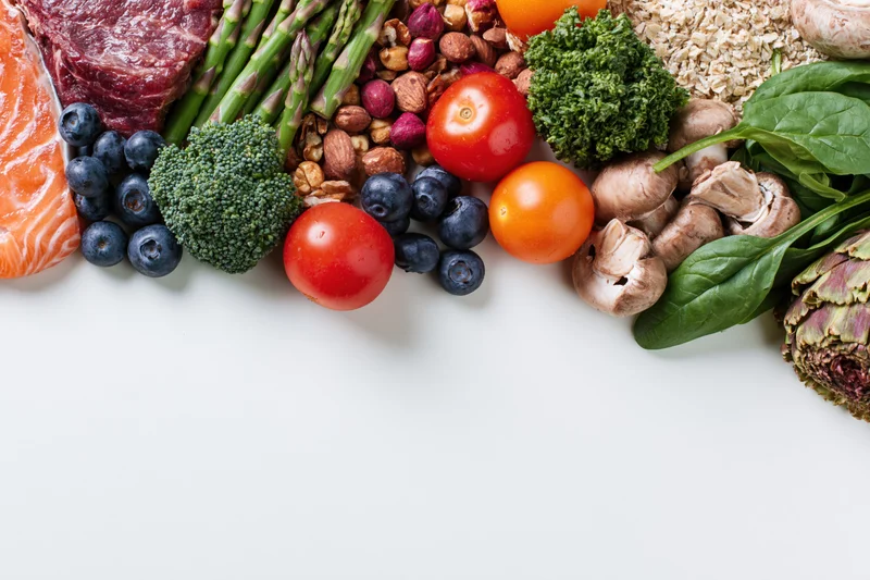 Assorted whole foods arranged along bottom edge of white surface