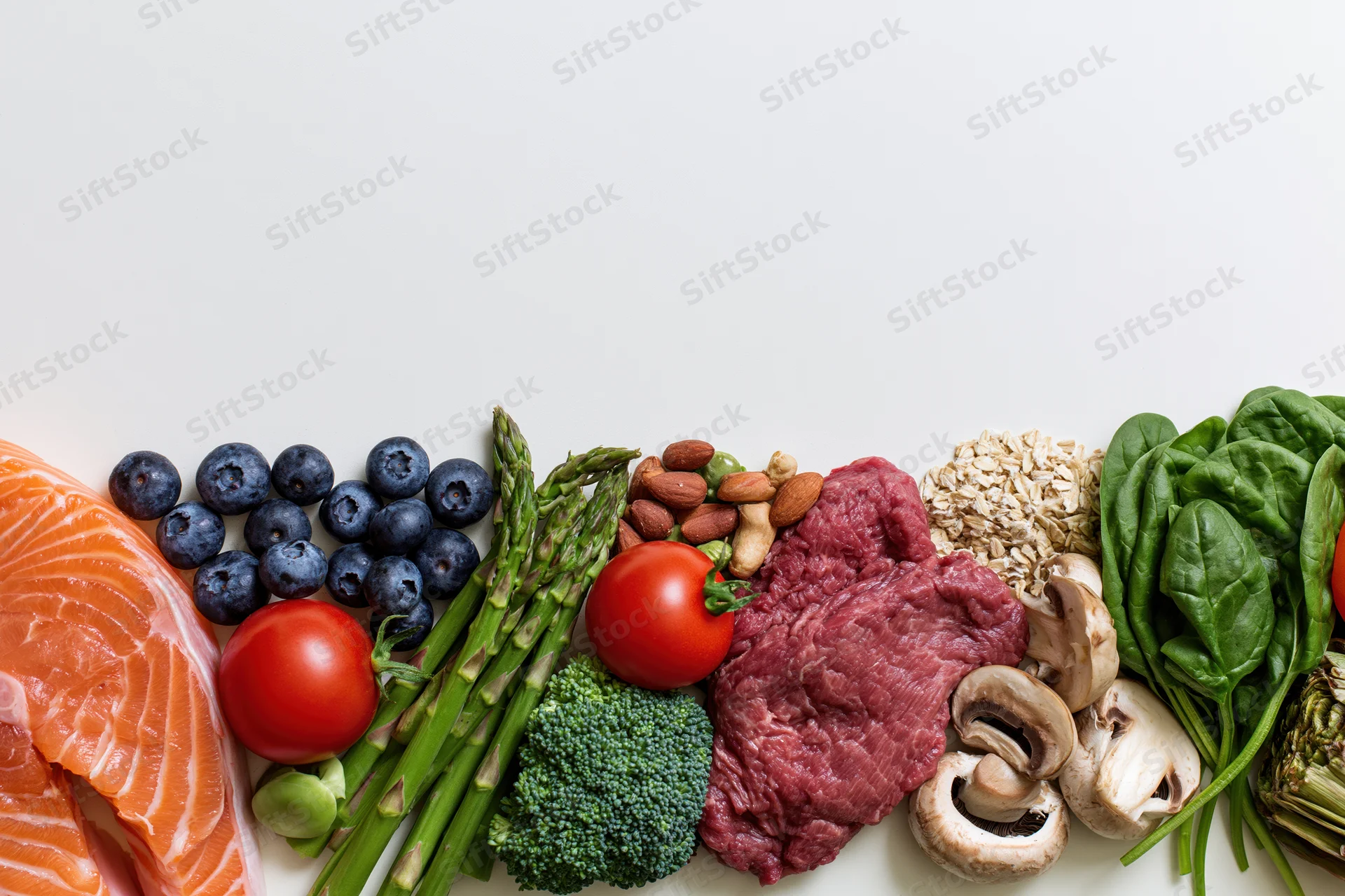 Assorted whole foods arranged along the bottom edge of a white surface with copyspace above