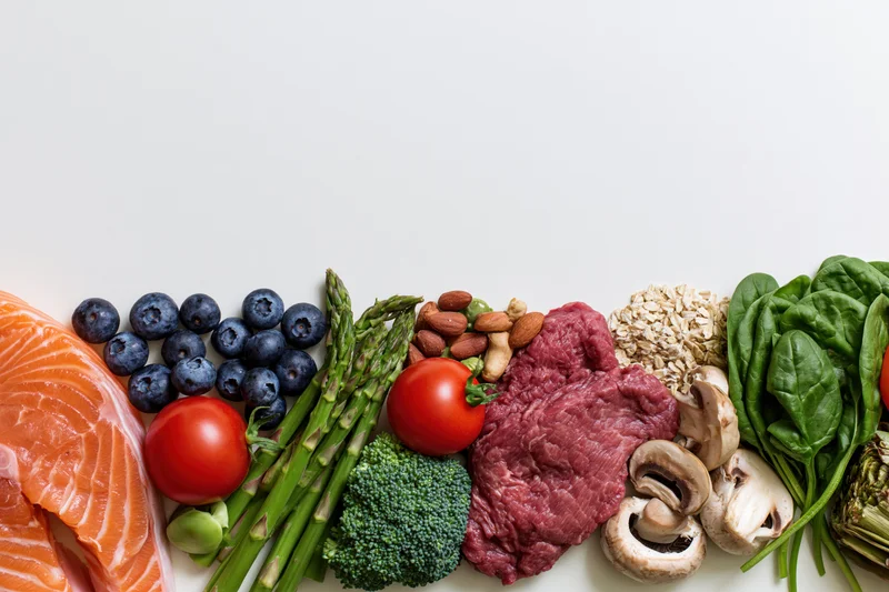 Assorted whole foods arranged along the bottom edge of a white surface with copyspace above