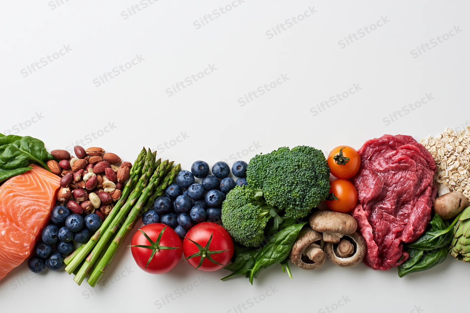 Assorted whole foods arranged in a row along the bottom edge of a white surface