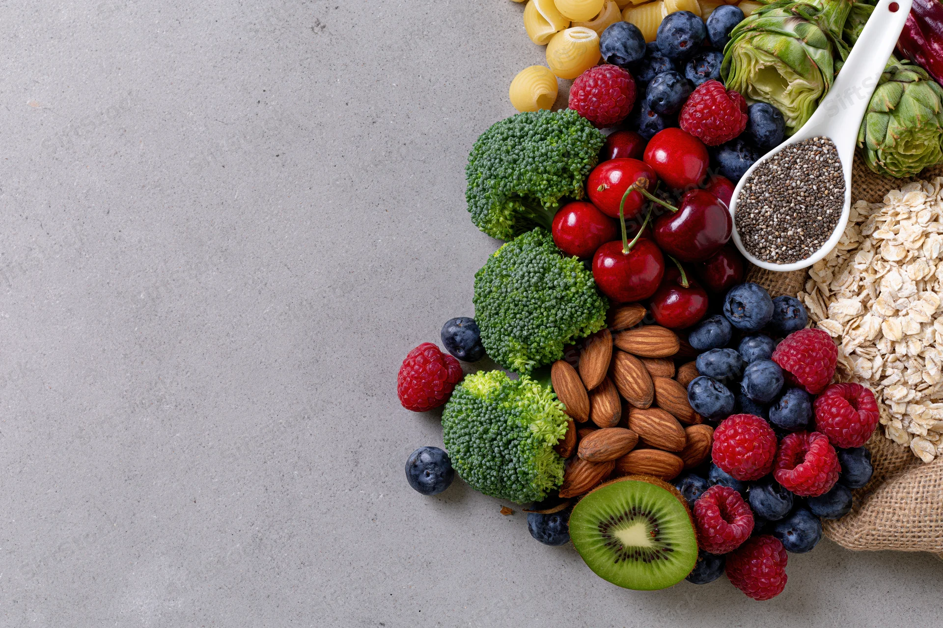 Assorted whole foods arranged diagonally on a gray stone countertop with copyspace
