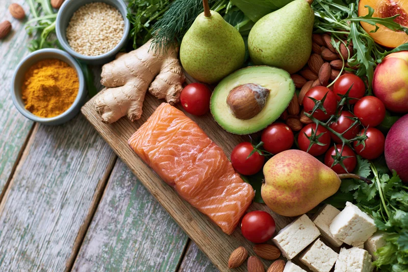 Salmon fillet and assorted fresh produce arranged on a wooden cutting board with spices and herbs