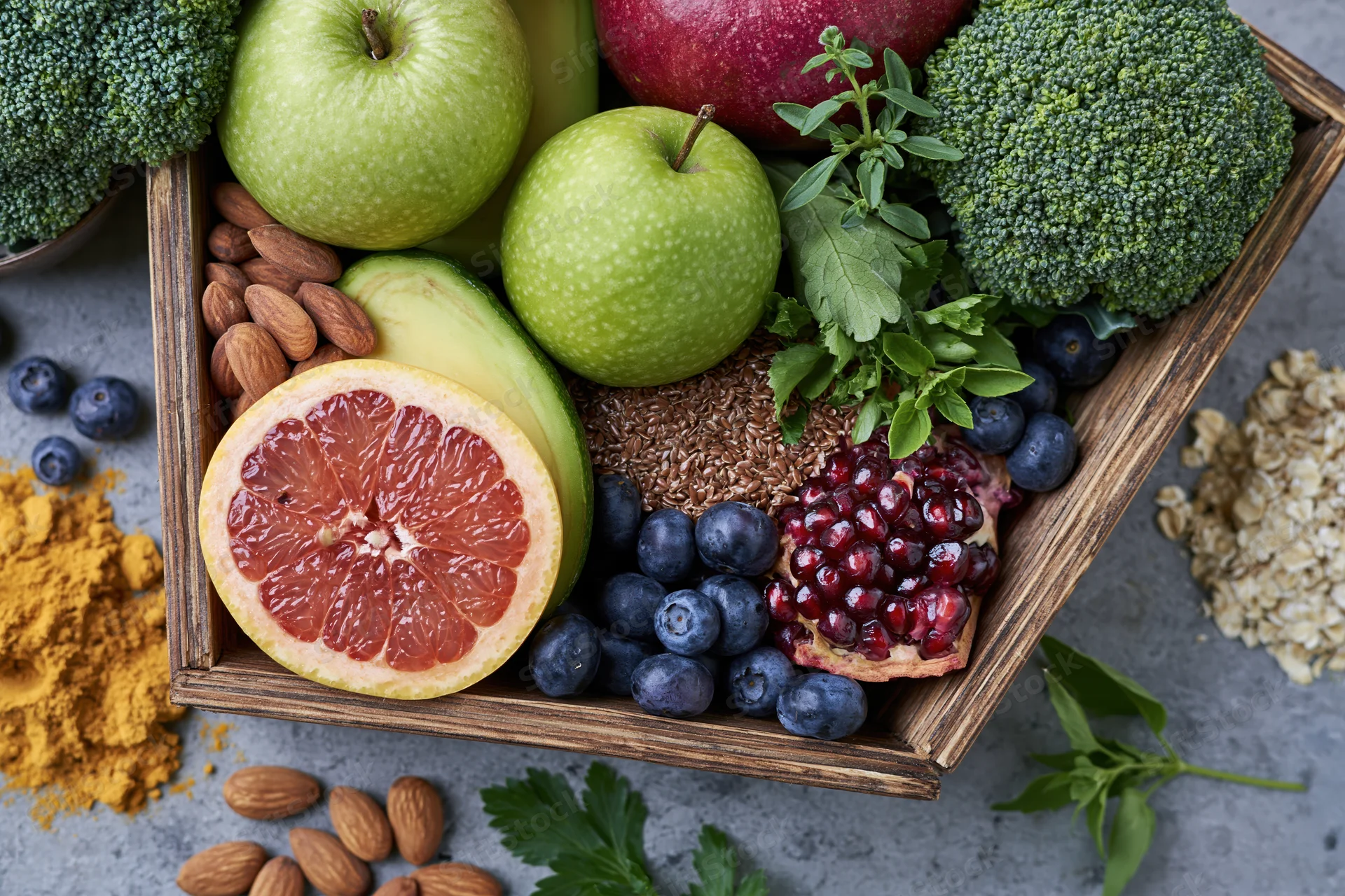 Fresh fruits and vegetables arranged in a wooden tray with nuts and spices on a stone surface