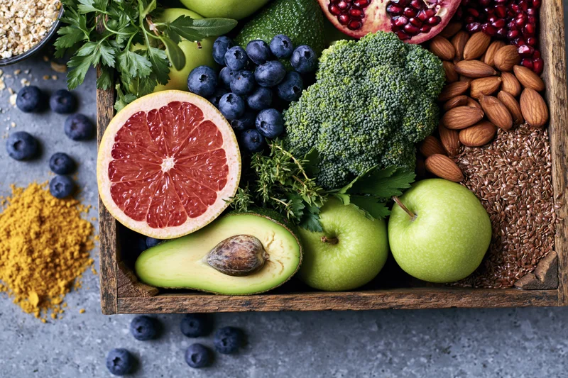 Fresh fruits and vegetables arranged in a rustic wooden tray on a gray countertop