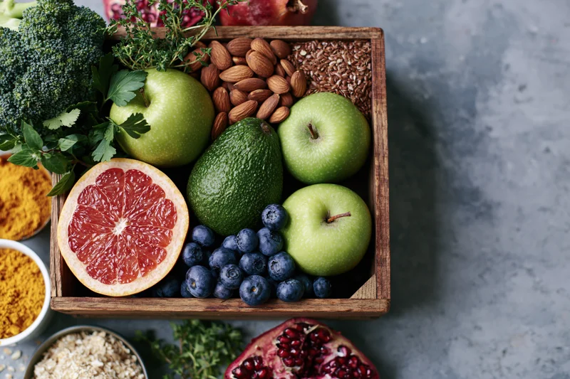 Fresh fruits and vegetables arranged in a wooden box on a gray countertop