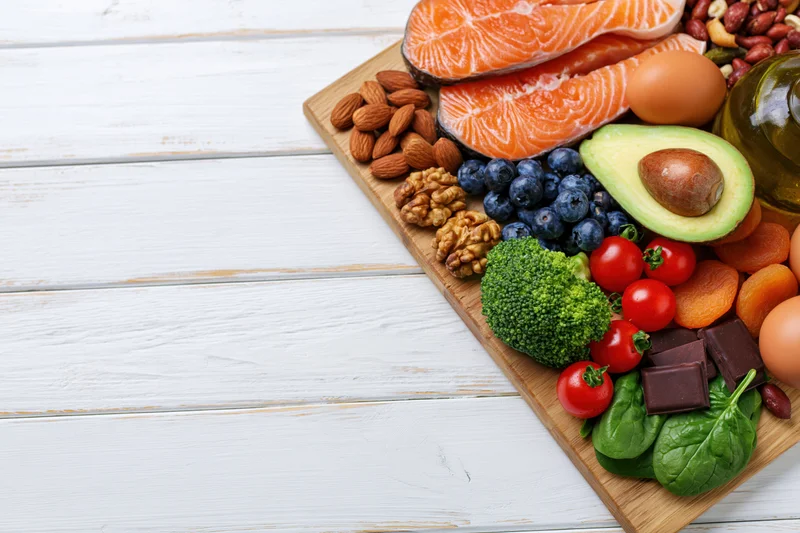 Healthy whole foods arranged on wooden board on white surface with copyspace