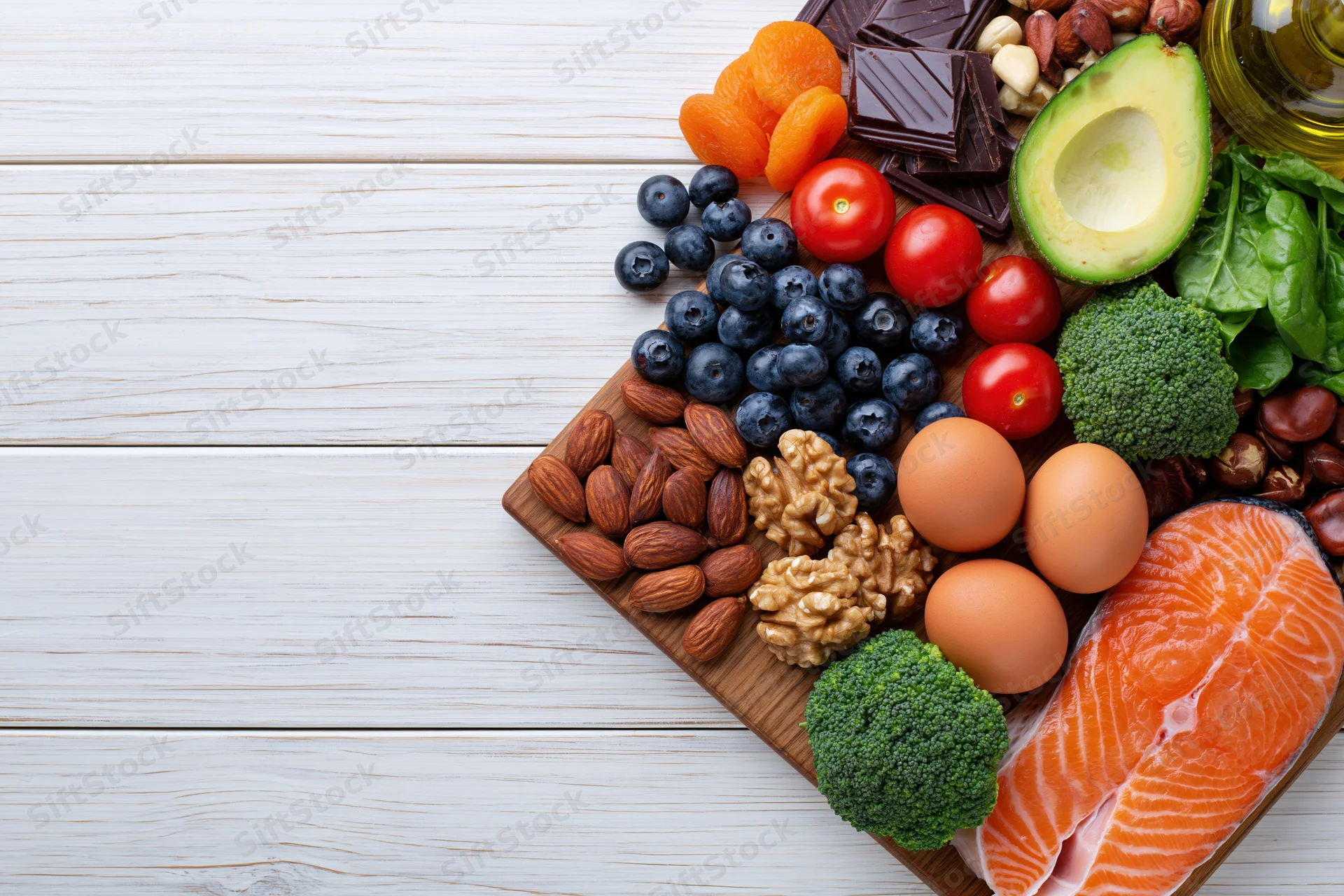 Assortment of healthy whole foods arranged on wooden board on white surface with copyspace