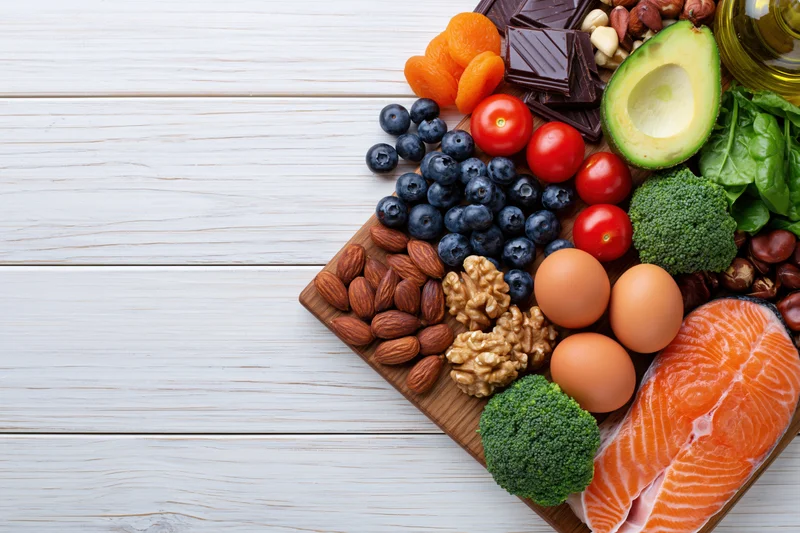 Assortment of healthy whole foods arranged on wooden board on white surface with copyspace