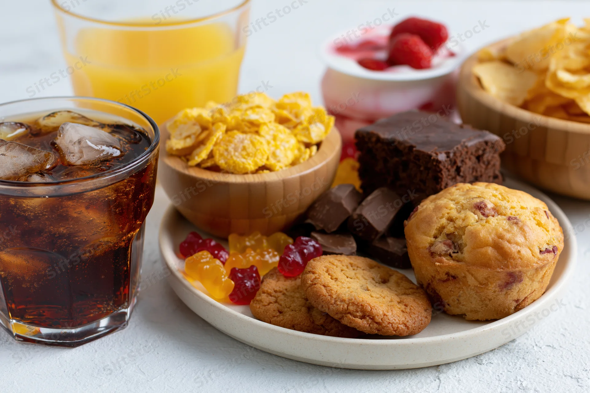 Assortment of sugary snacks and processed foods arranged on a plate with drinks