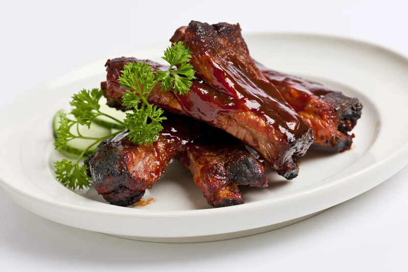 Glazed pork ribs with parsley and cucumber on a white plate
