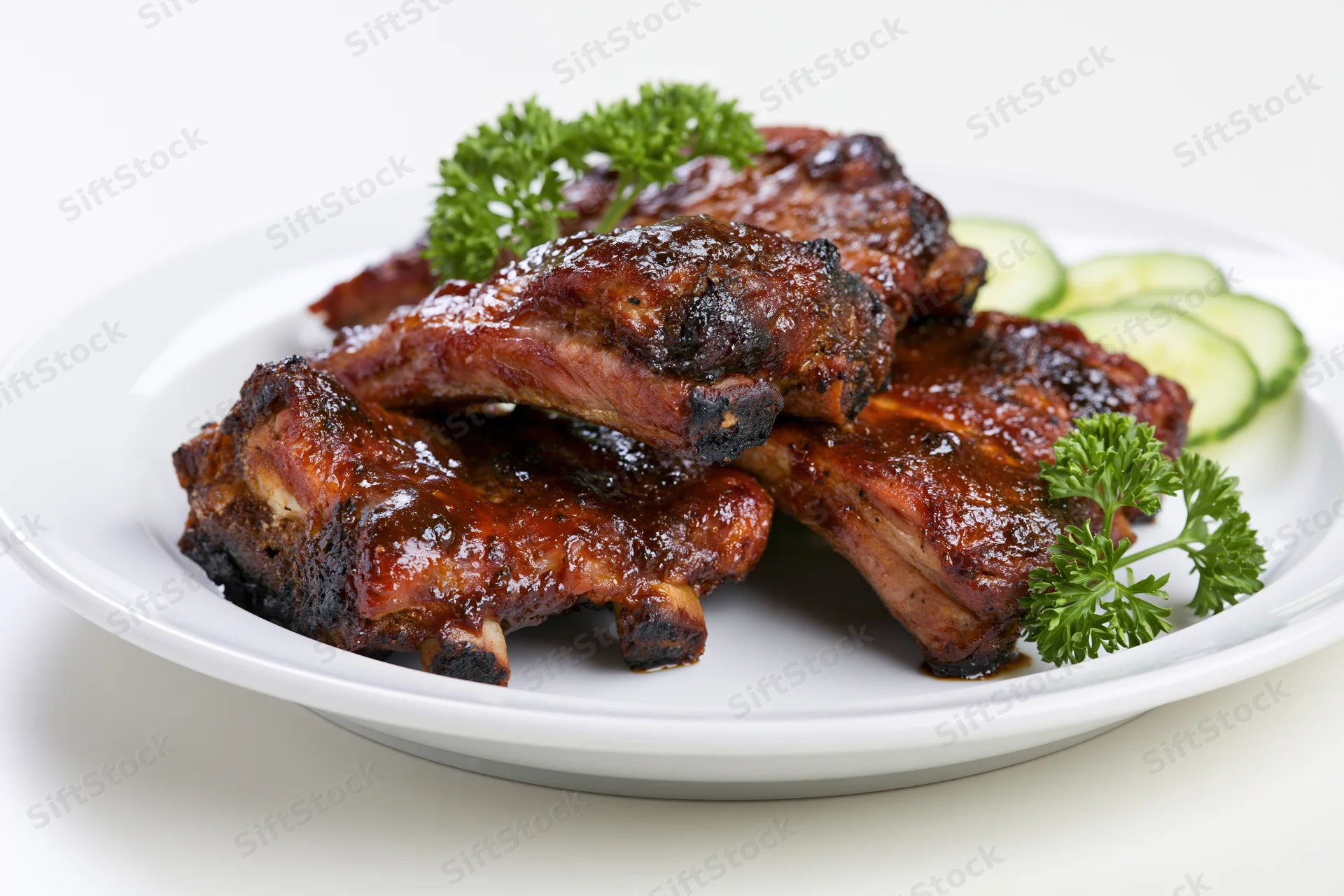 Glazed barbecue pork ribs on a white plate with parsley and cucumber garnish